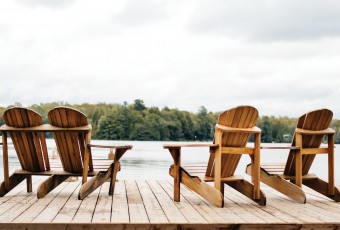 Adirondack Chairs at the end of a pier overlooking a large blue lake with a blue sky