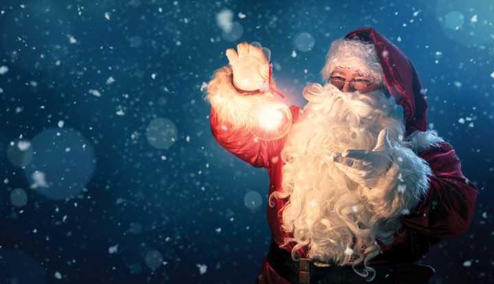 Happy Santa Claus holding glowing christmas ball over defocused blue background with copy space